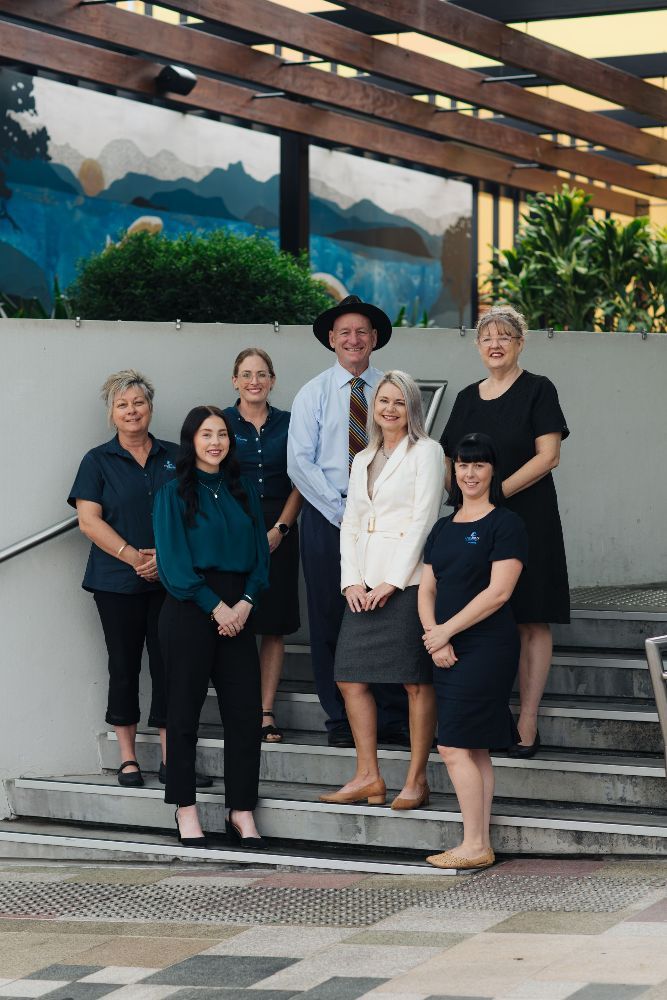 Group of eight people standing on outdoor steps. Most are smiling, wearing business attire, with a blue mural in the background.— Chris Trevor & Associates in Gladstone Central, QLD