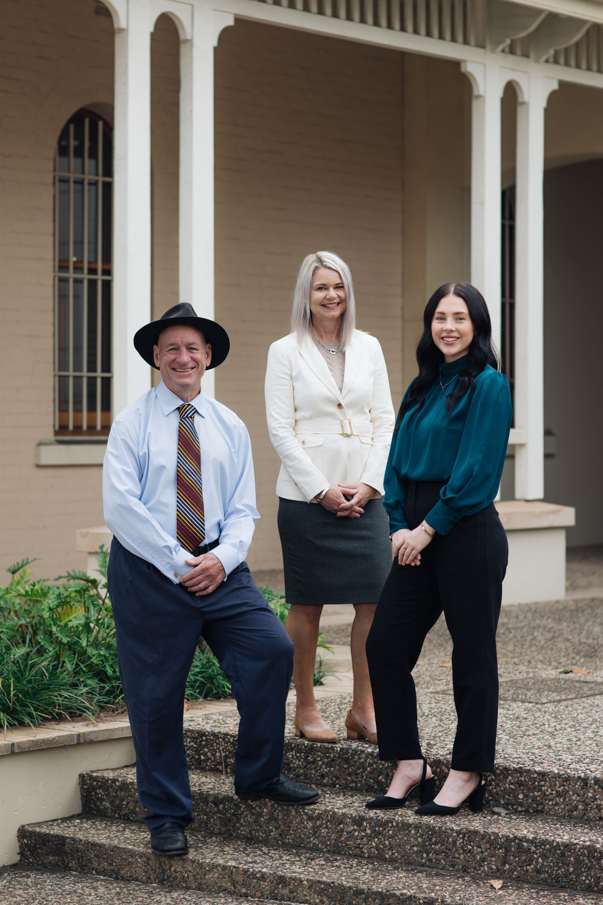 Group of eight people standing on outdoor steps. Most are smiling, wearing business attire, with a blue mural in the background.— Chris Trevor & Associates in Gladstone Central, QLD