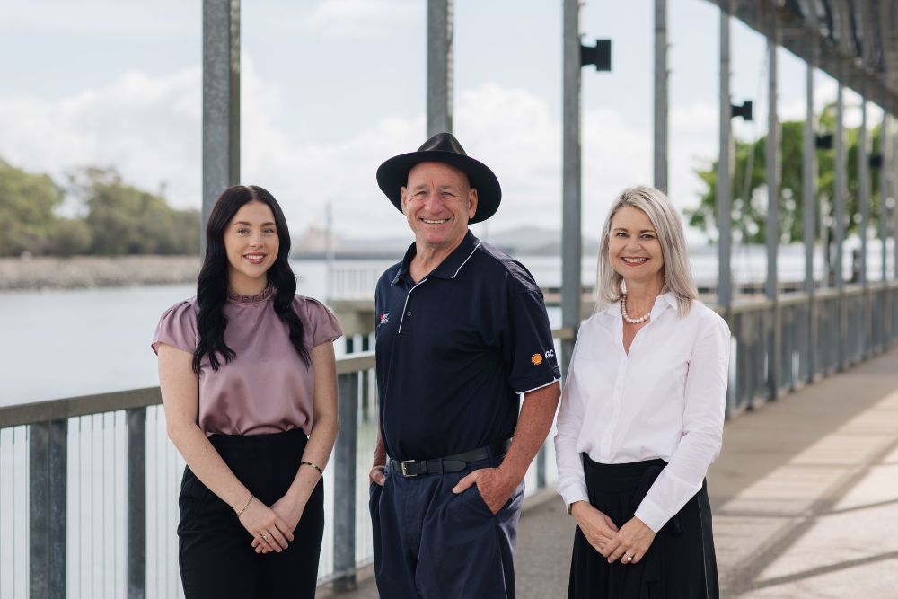 Three people standing outdoors near a body of water. A woman on the left, one man in the middle wearing a hat, and another woman on the right, all smiling.— Chris Trevor & Associates in Gladstone Central, QLD