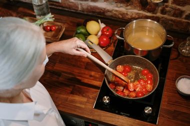 A woman is stirring tomatoes in a pan on a stove.