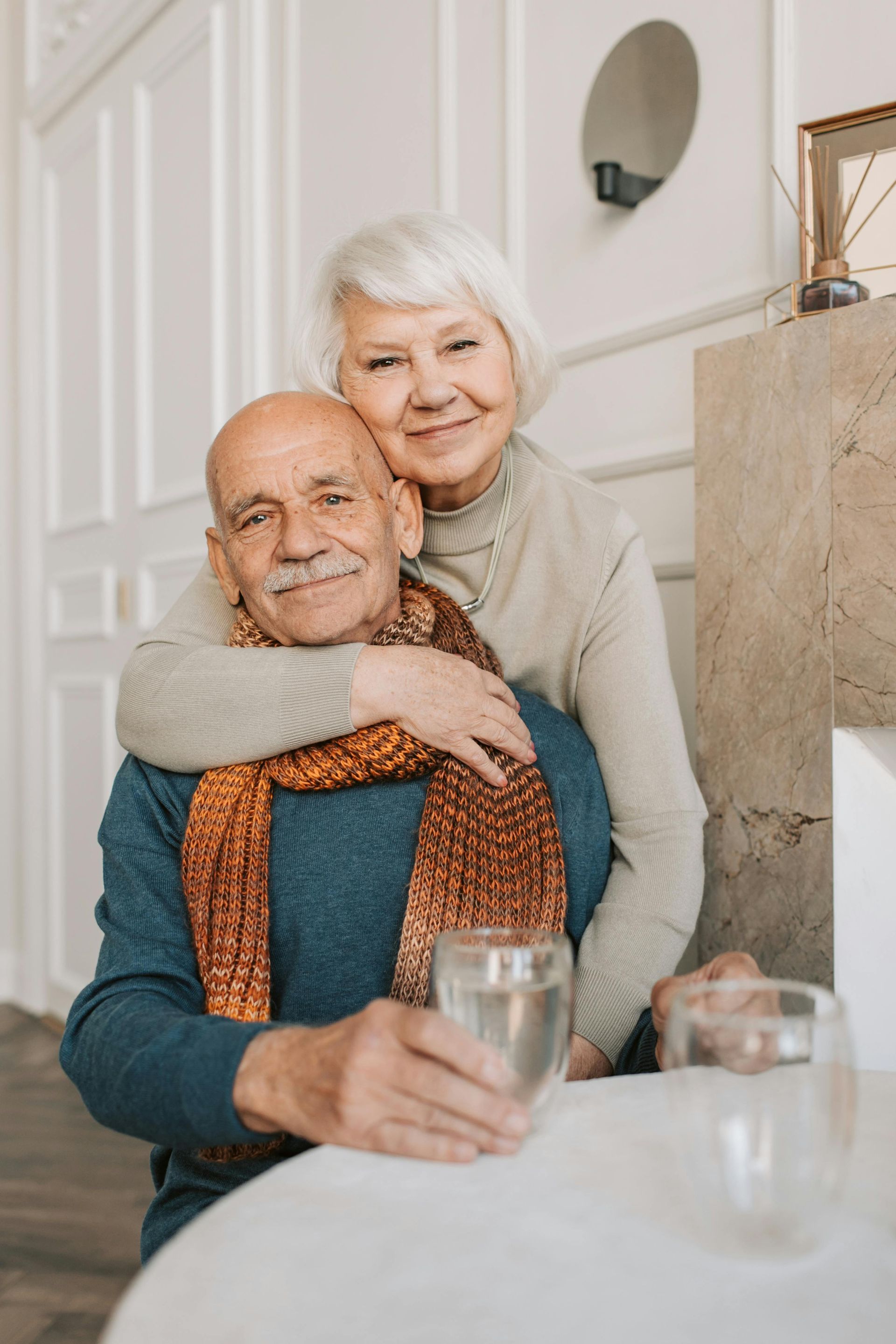 An elderly couple is sitting at a table with a glass of water.