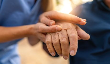 A nurse is holding the hand of an elderly woman.