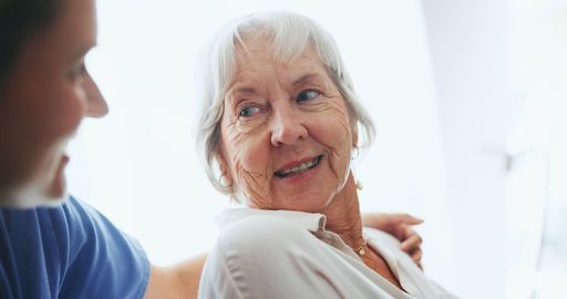 An elderly woman is smiling while talking to a nurse.