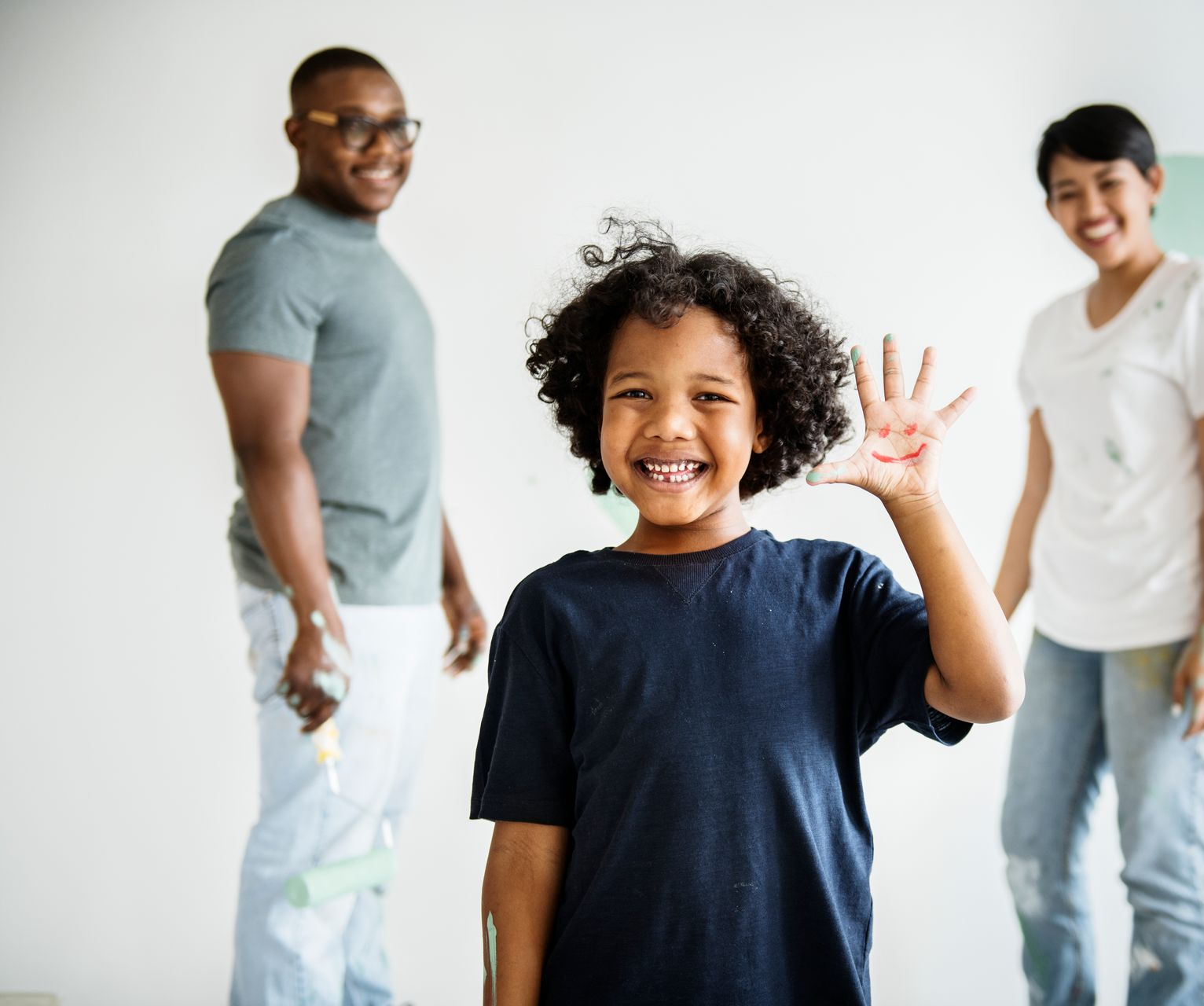 A young boy is waving at the camera while standing next to a man and woman.