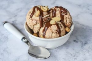 A bowl of ice cream with nuts and chocolate sauce next to a spoon.