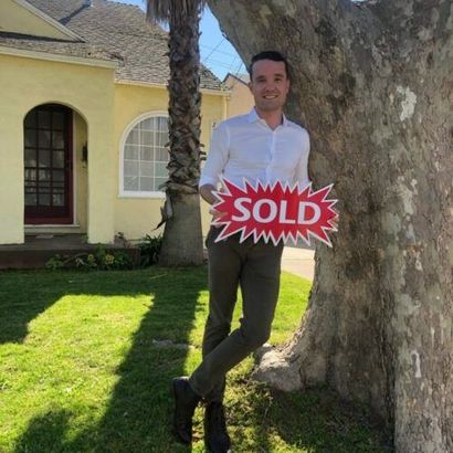 A man is holding a sold sign in front of a house