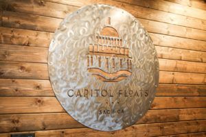 A metal sign on a wooden wall that says capitol floats.