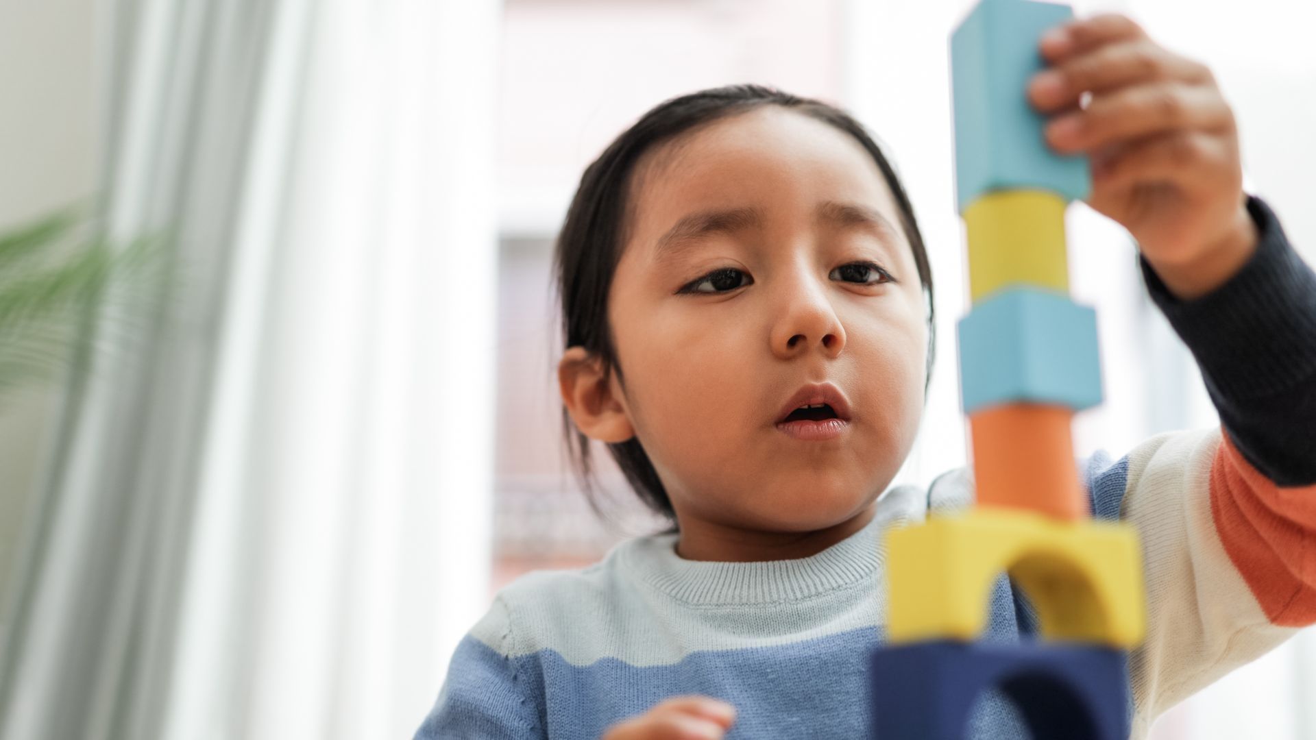 A little girl is playing with wooden blocks in a living room.