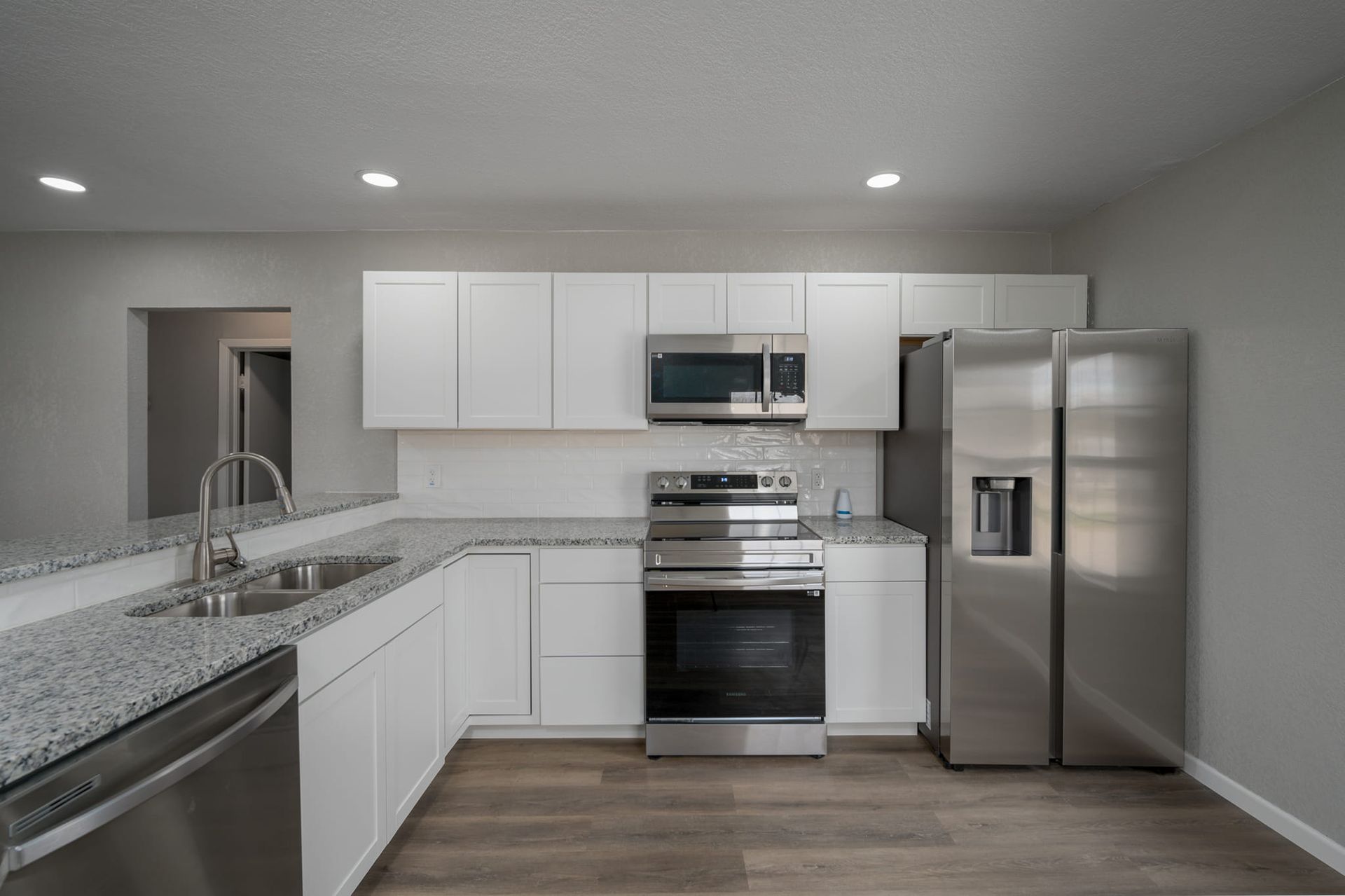 An empty kitchen with stainless steel appliances and white cabinets.