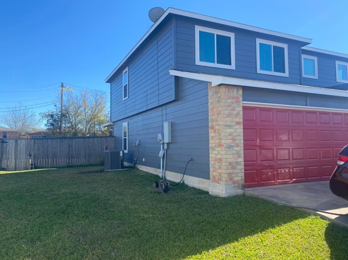 A car is parked in front of a house with a red garage door.