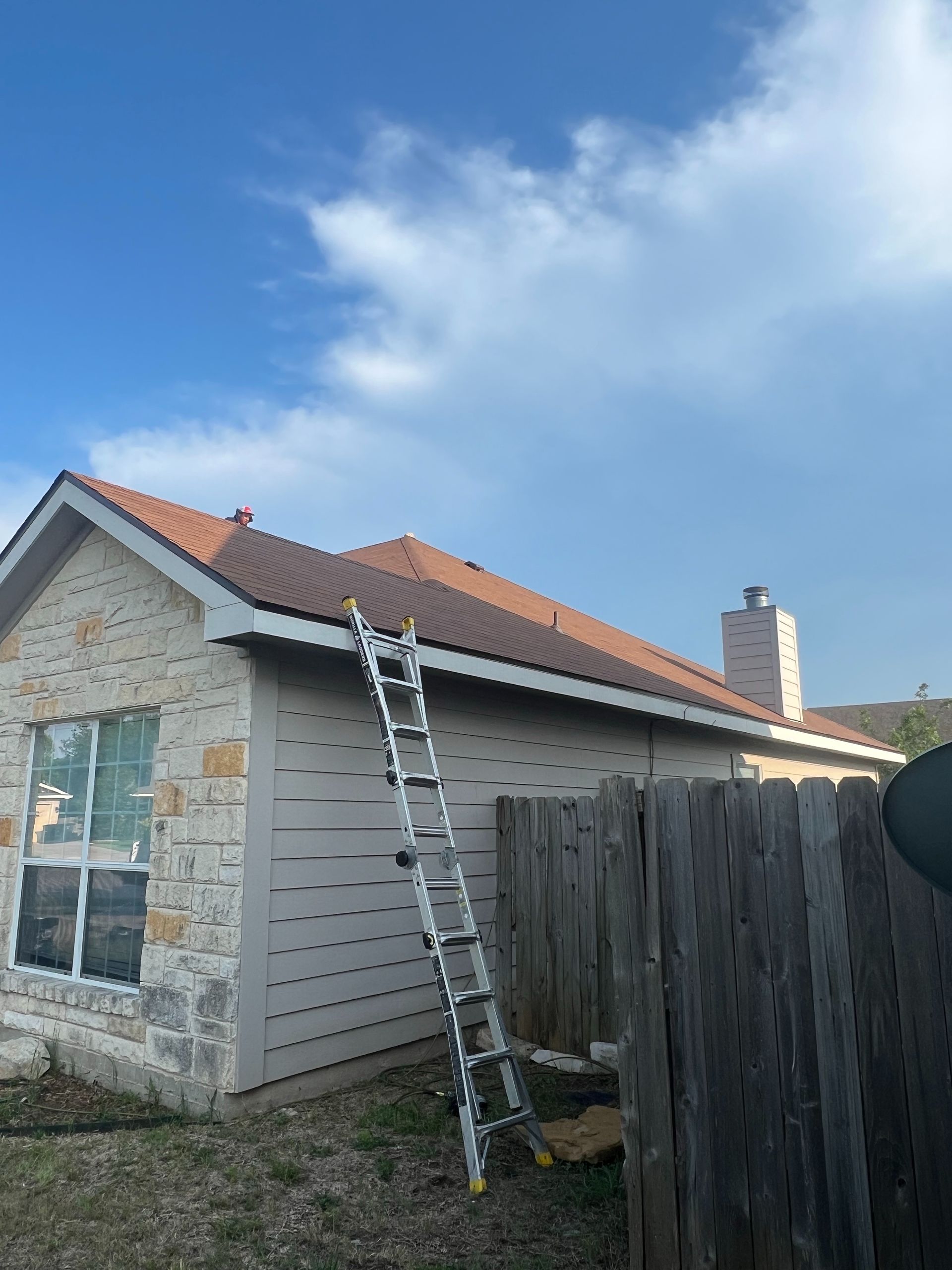 A ladder is sitting on the side of a house next to a wooden fence.