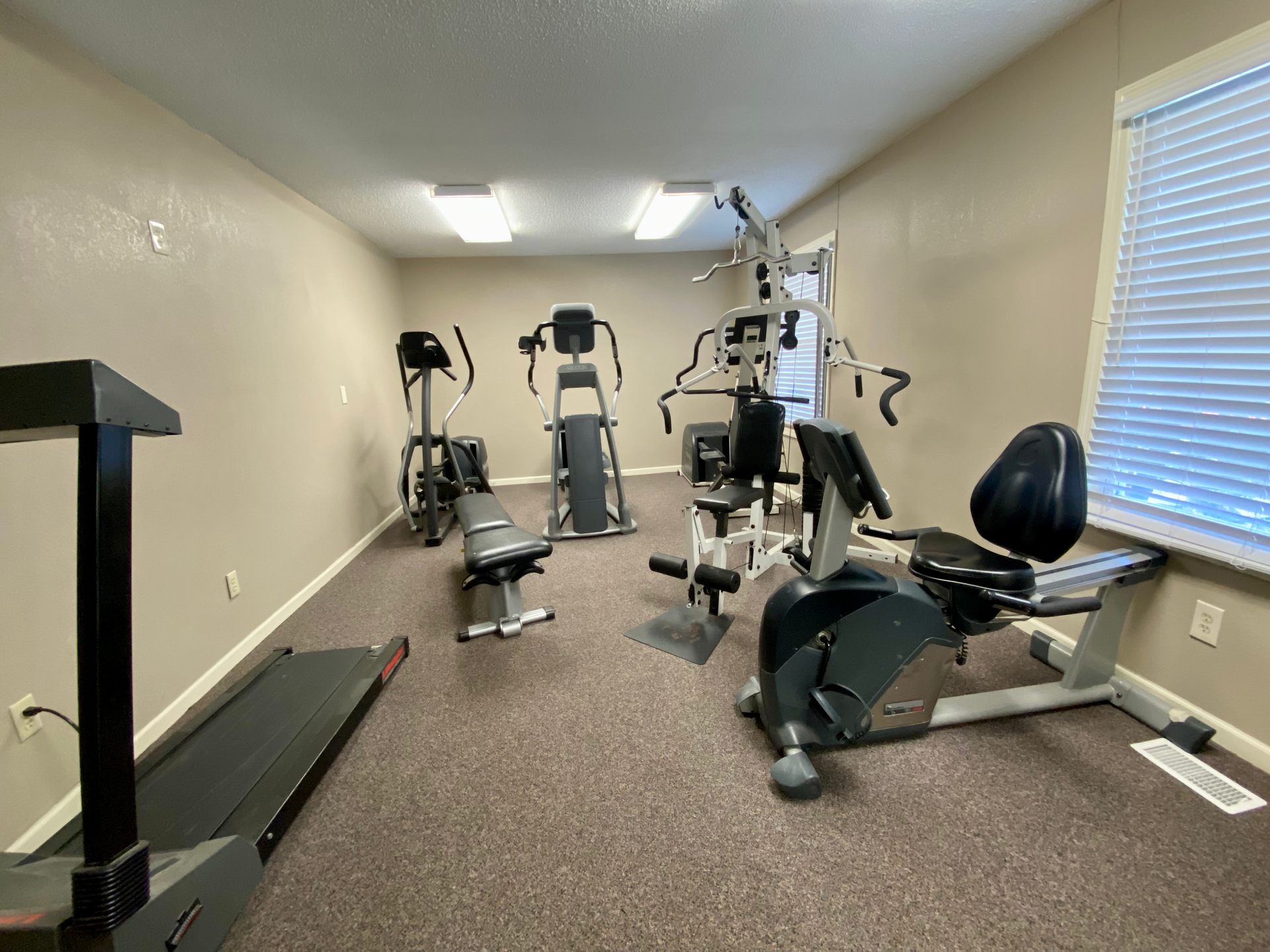 Small home gym with treadmill, exercise bikes, and weight machine.
