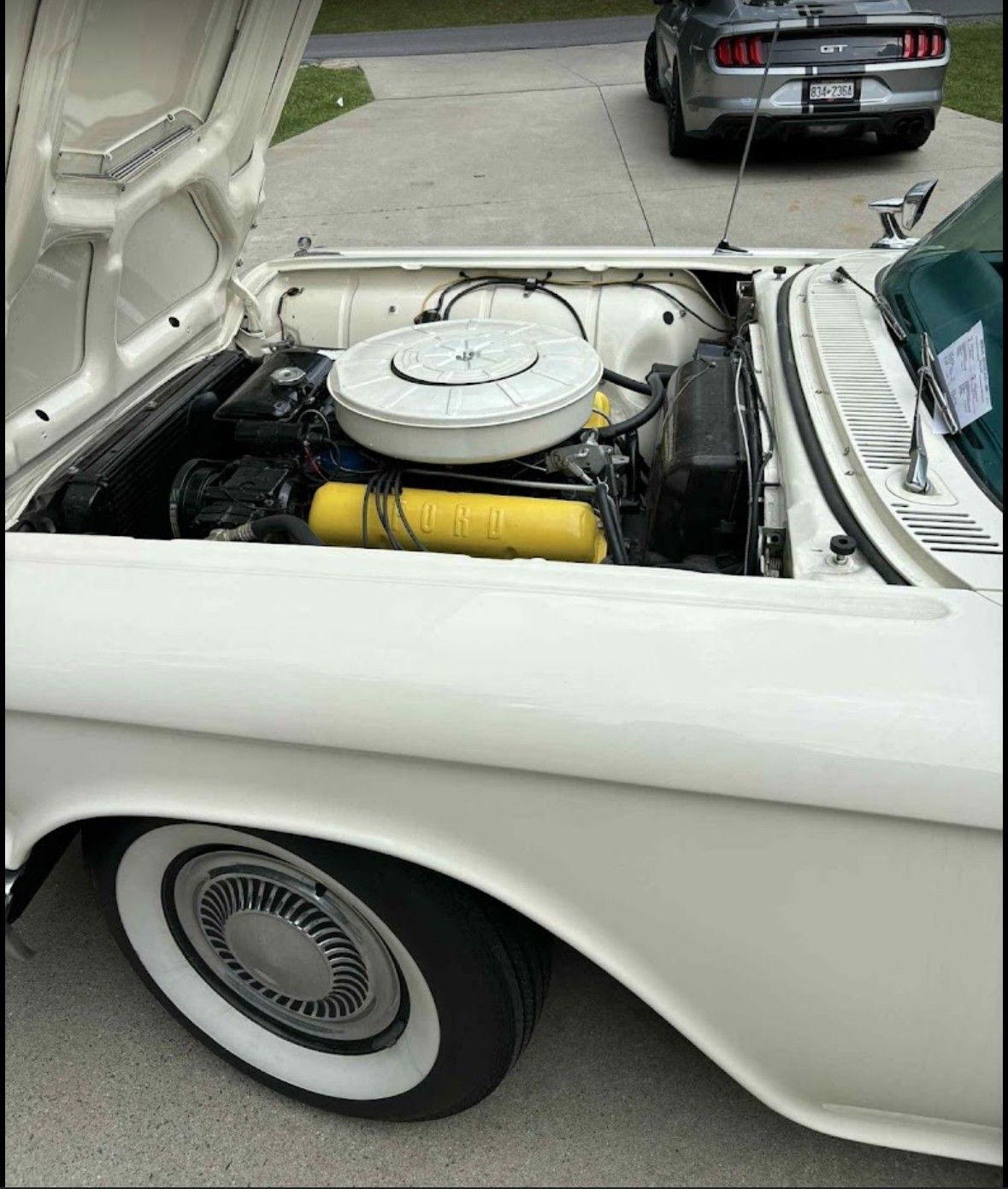 White classic car with open hood, engine visible, white tire rims, and modern car in background.