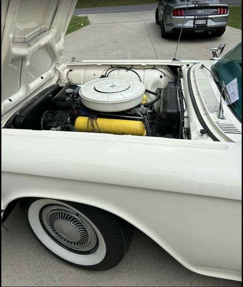 White classic car with open hood, engine visible, white tire rims, and modern car in background.
