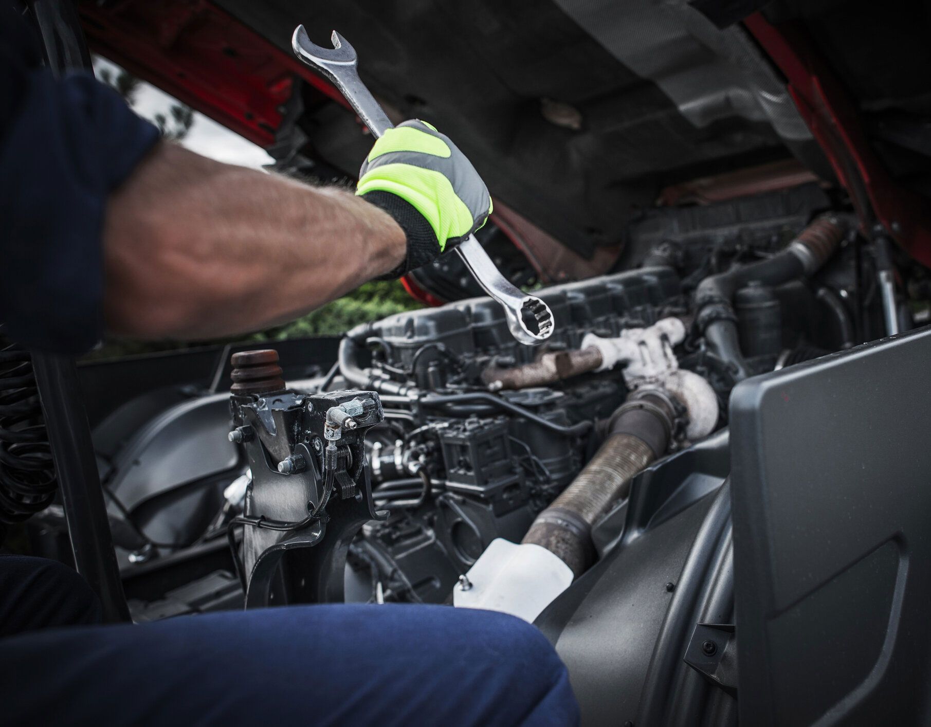 Mechanic working on an engine with a wrench, wearing gloves.
