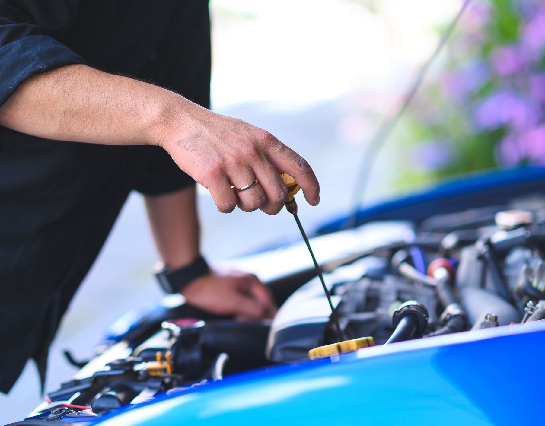 Person checking car oil with dipstick in an open engine bay. Blue car and black shirt visible.