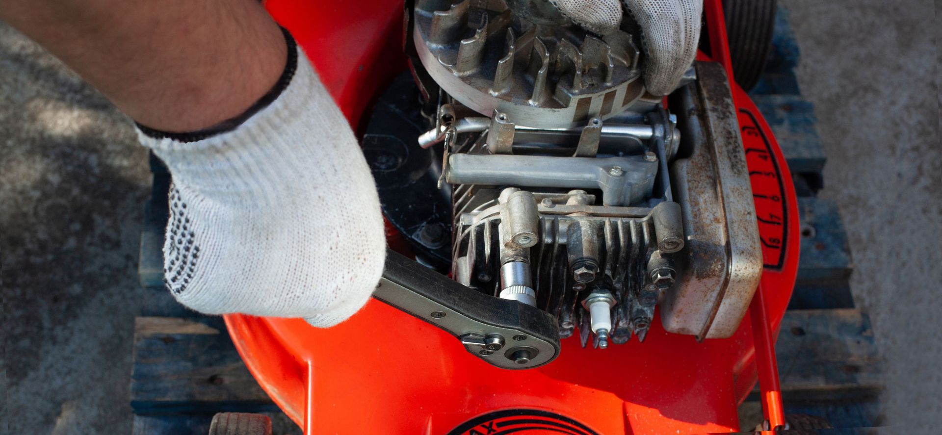 A gloved hand uses a wrench on a lawnmower engine.