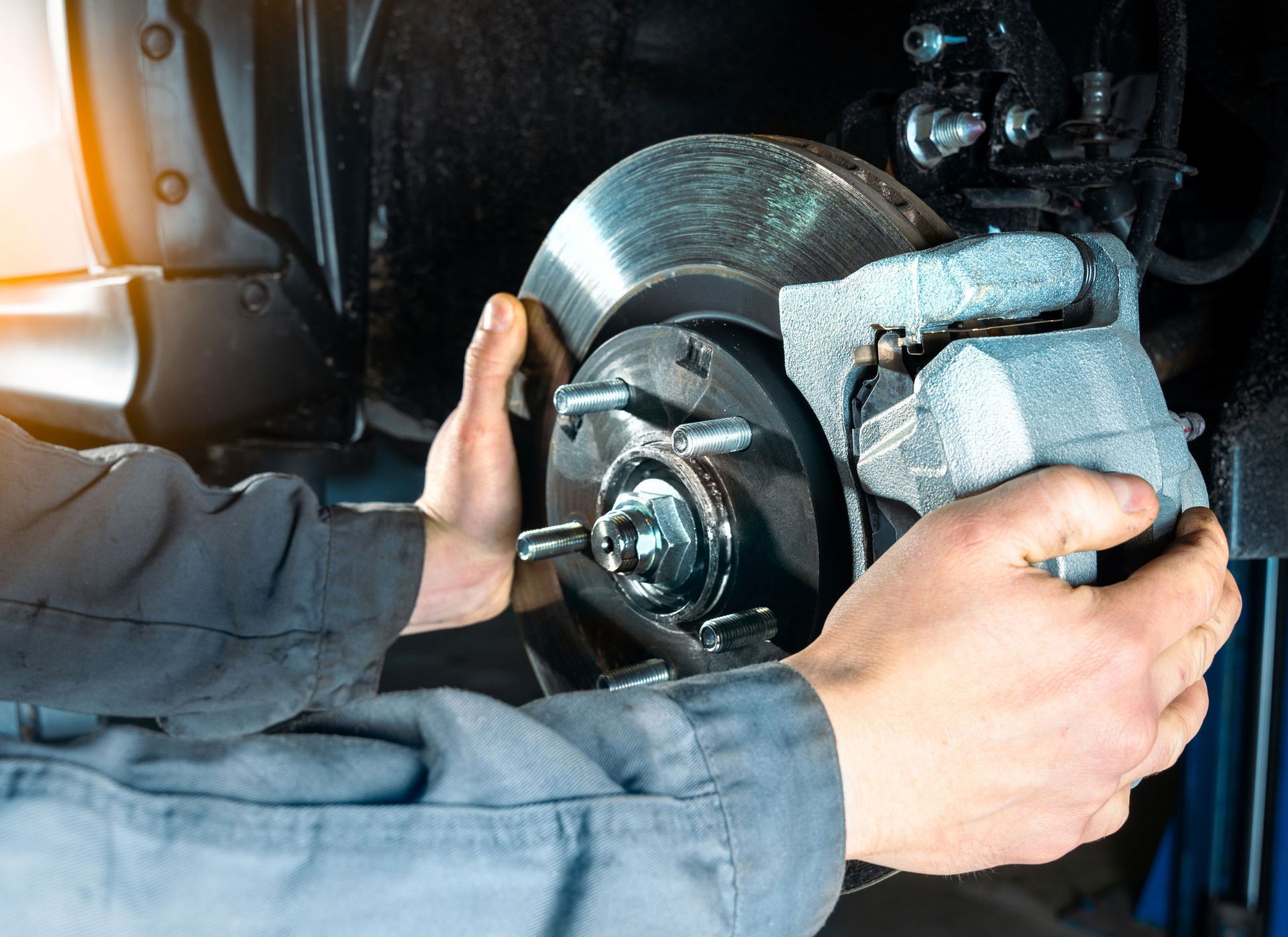 Mechanic working on a car's brake disc assembly, hands visible, in a repair shop.