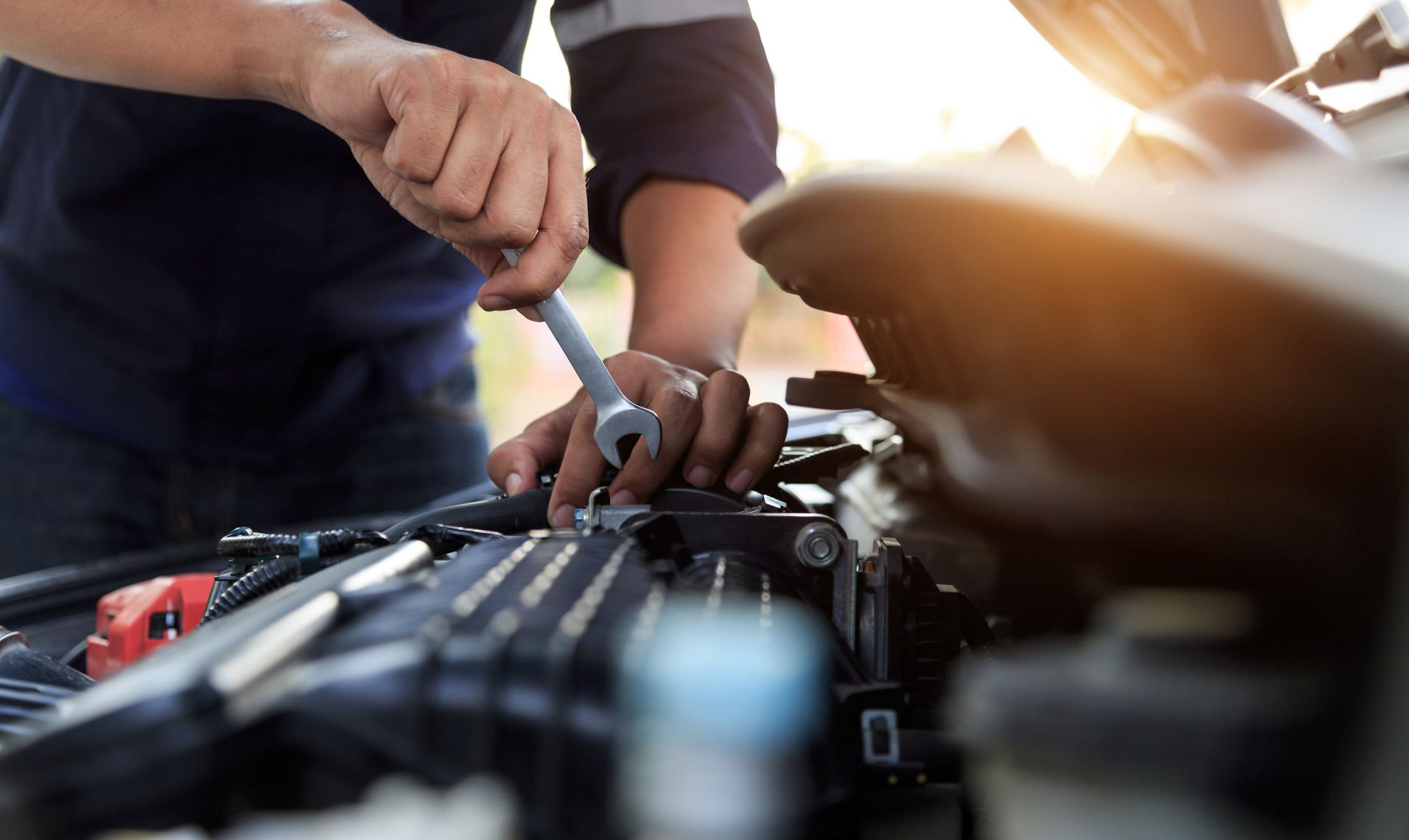 Person using a wrench on a car engine, outdoors.