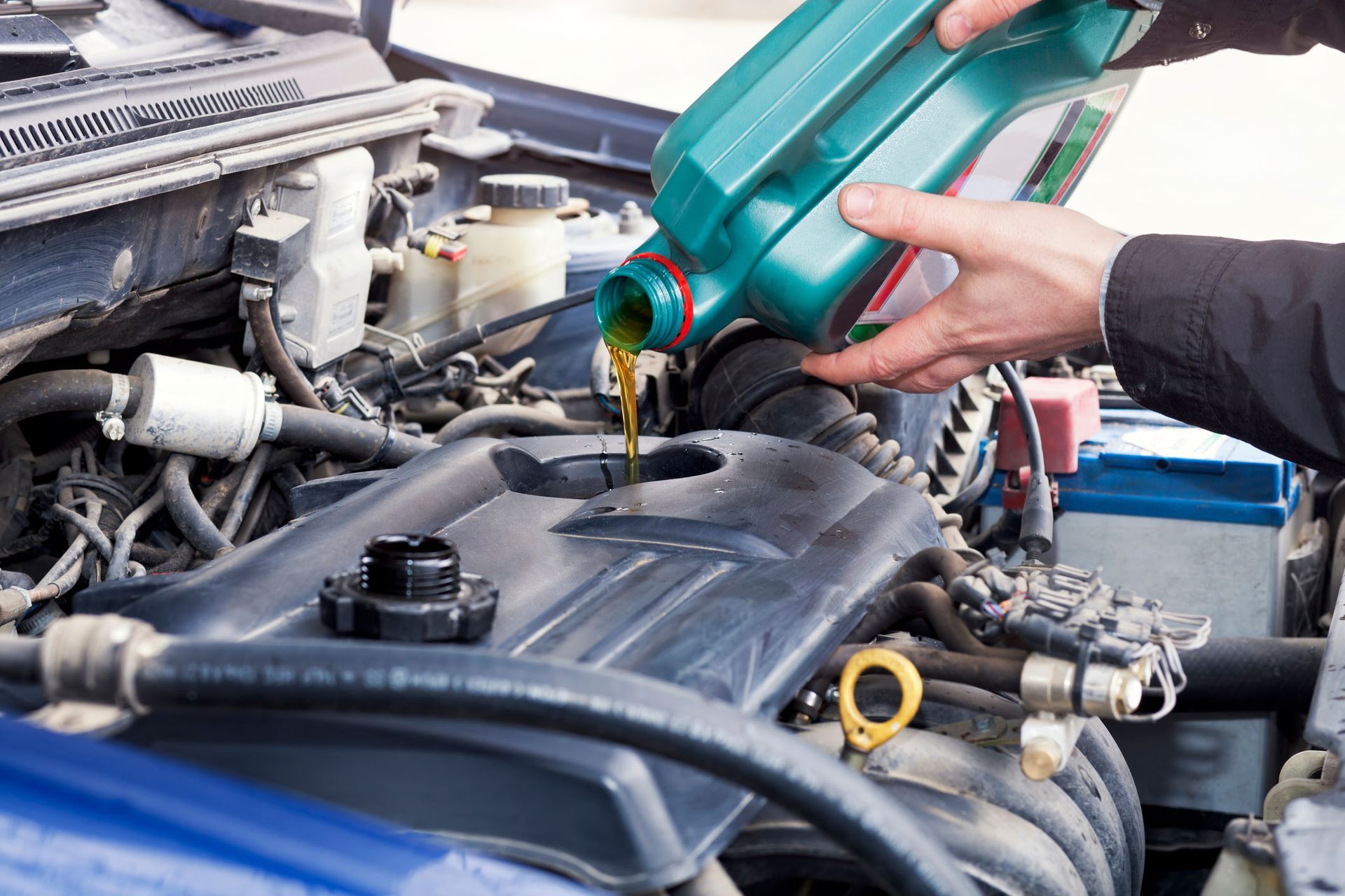 Person pouring oil into a car engine from a green bottle.