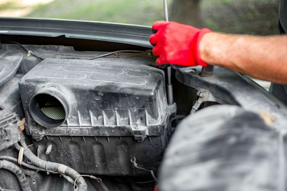 Person in red gloves, working on a car engine, lifting the hood.