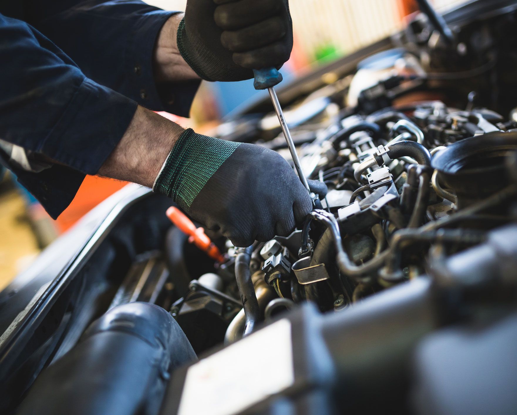 Mechanic in black gloves working on a car engine with a screwdriver.
