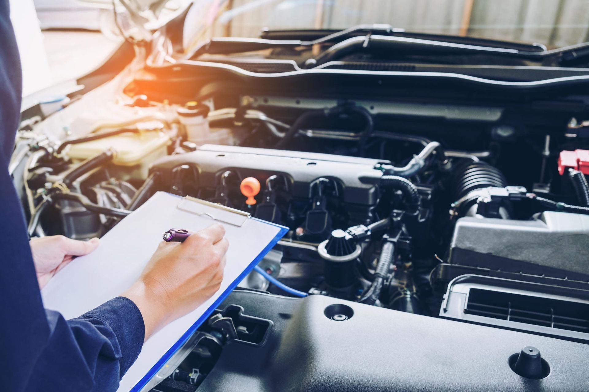 Mechanic inspecting a car engine, holding clipboard and pen.