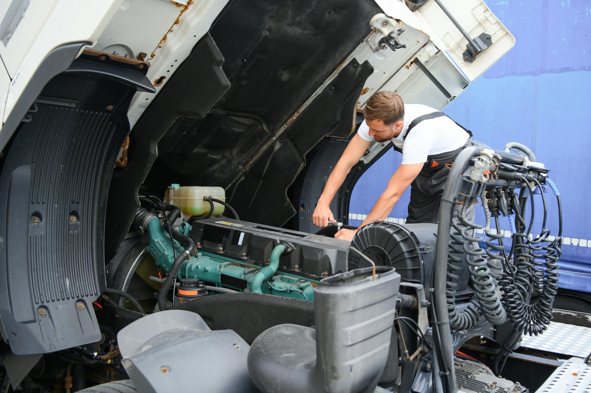Mechanic working on the engine of a truck with the hood open.