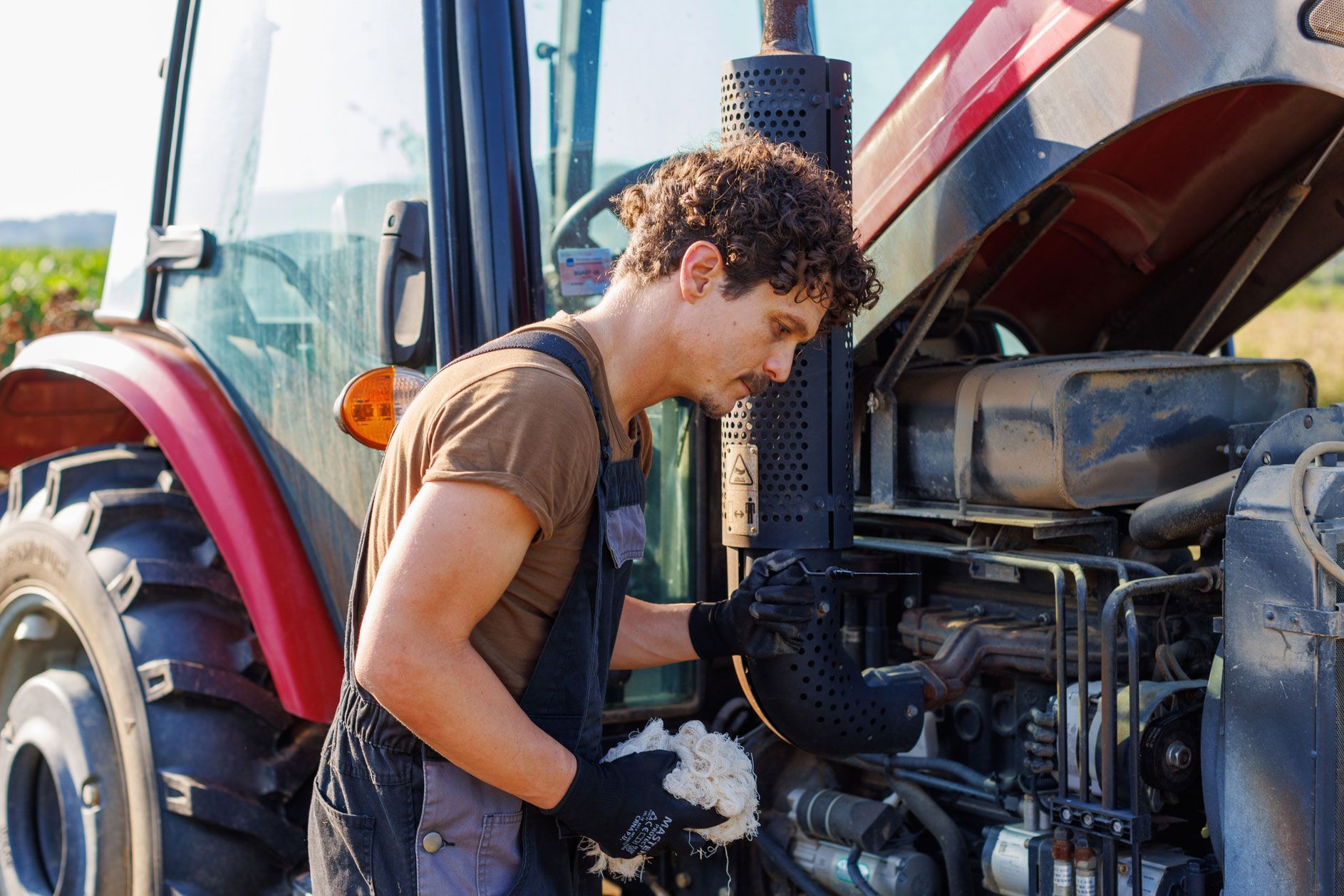Man in overalls repairs a red tractor engine in a field.