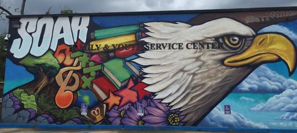 Mural on a wall. It depicts an eagle's head, books, music notes, stars, and flowers with the word 