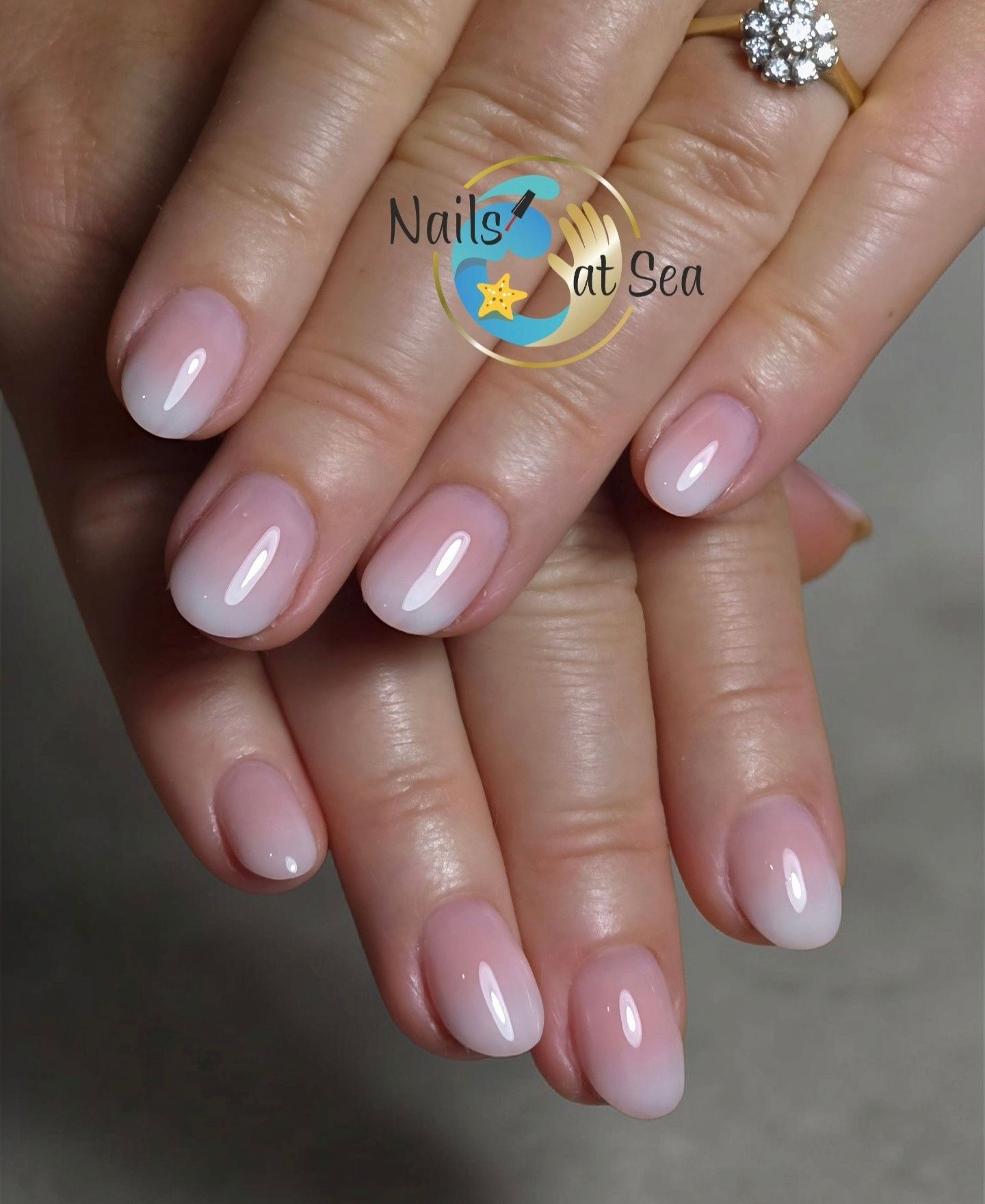 Verzorgde vingernagels met een zachtroze en witte ombre-kleurovergang, weergegeven op gevouwen handen.