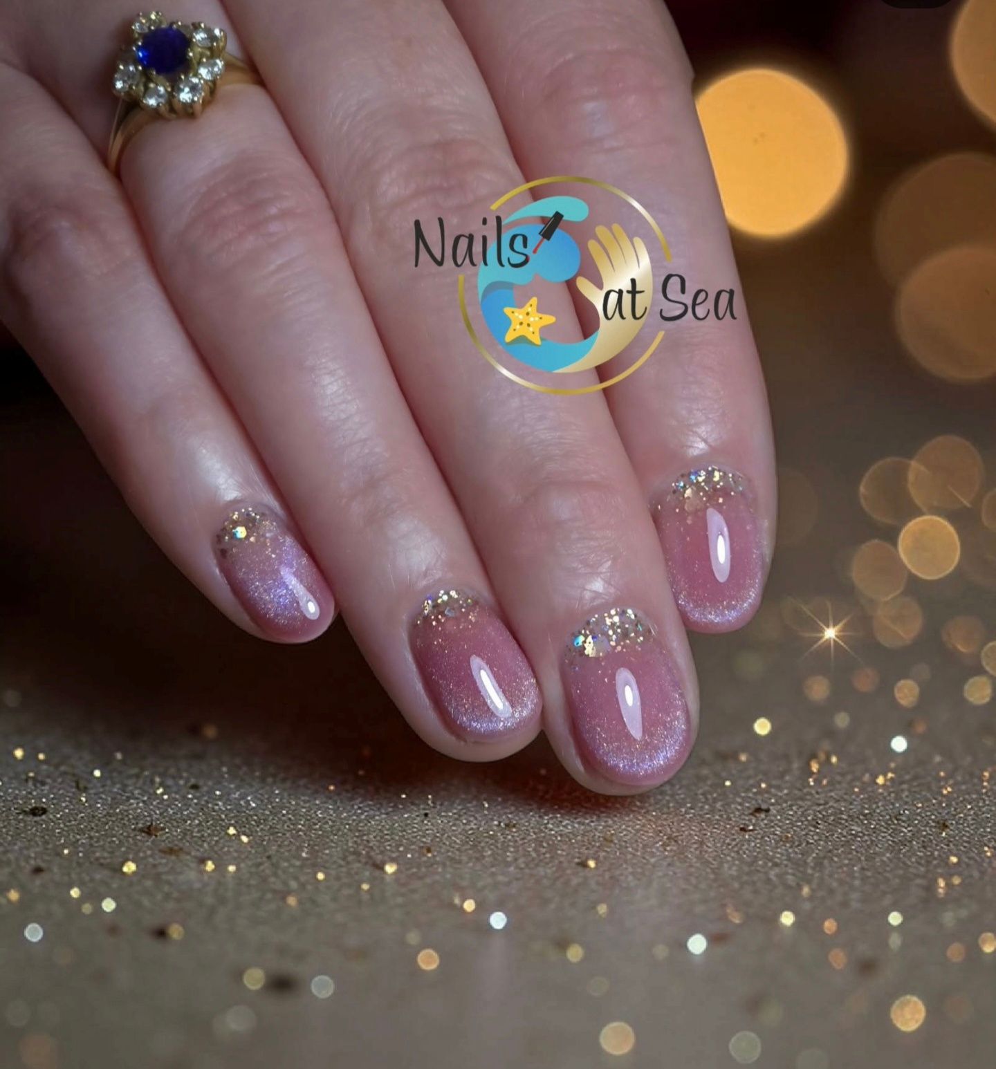 Een hand met roze, magnetische nagels, elk versierd met een klein rijtje kristallen aan de basis, tegen een bokeh-achtergrond.
