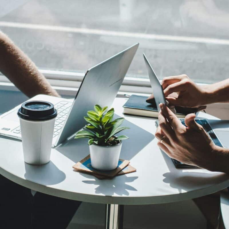 Two people are sitting at a table using laptops and tablets