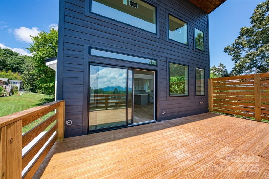 Exterior of a modern house with a wooden deck and sliding glass door, against a mountain backdrop.