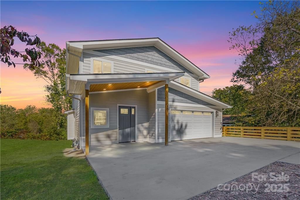 Two-story house with gray siding, attached garage, and a driveway at sunset.