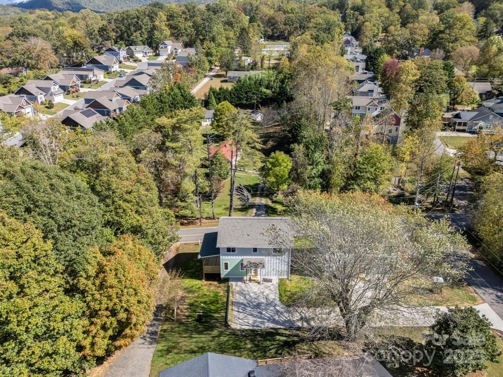 Aerial view of a light blue house surrounded by trees and residential neighborhood in autumn.