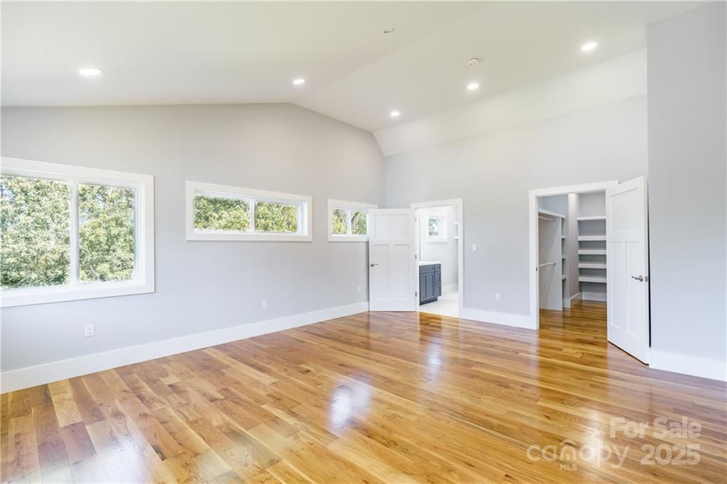 Spacious bedroom with hardwood floors, windows, and white walls, leading to a bathroom and closet.
