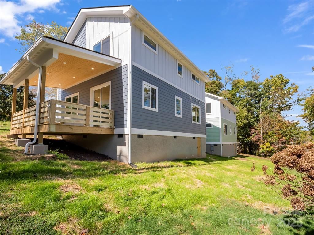 Two-story modern home with light blue, gray, and white siding. Wooden porch and grassy yard.
