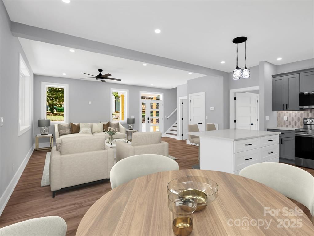 Modern home interior with living room, dining area, and kitchen. Soft gray walls, light furniture, hardwood floors.