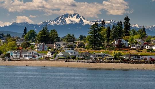 A small town on the shore of a lake with mountains in the background.