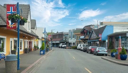 A row of cars are parked on the side of a street in a small town.