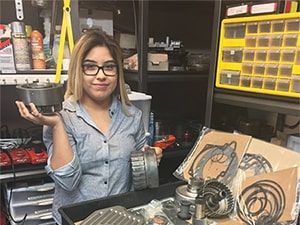 A woman is holding a piece of metal in her hands in a garage. | Aus Tex Transmissions