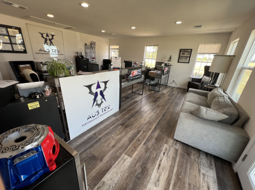 Office interior with wood floors, a reception desk with logo, a sofa, and display items. | Aus Tex Transmission