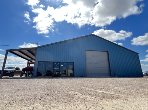 Blue metal building with a covered awning, roll-up door, and signage under a cloudy sky. | Aus Tex Transmission