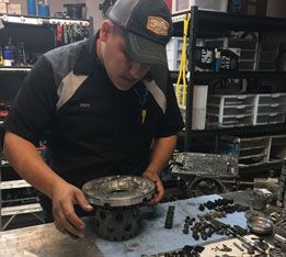 A man is working on a piece of metal in a garage. | Aus Tex Transmissions
