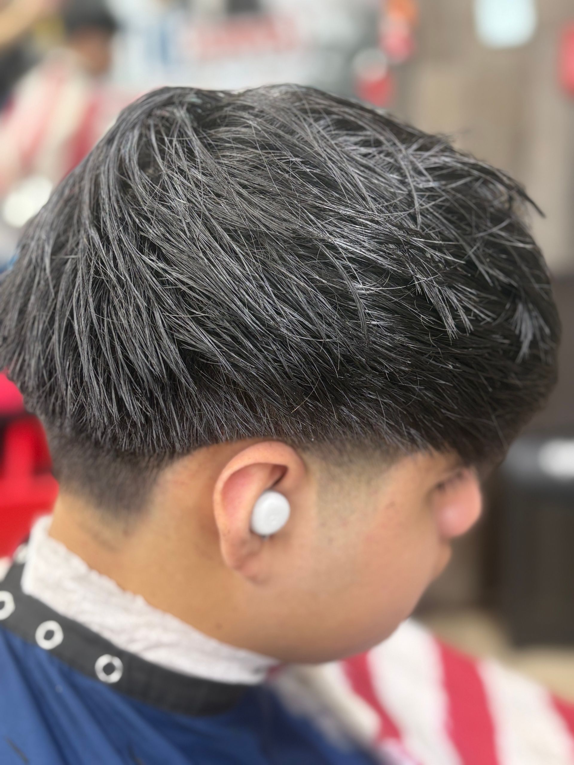 Barber giving a man a fade haircut with electric clippers in a salon.