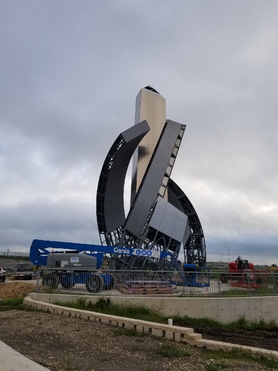 Starship prototype on a launch mount, surrounded by construction equipment. The shiny silver rocket is partially obscured by black launch tower arms.