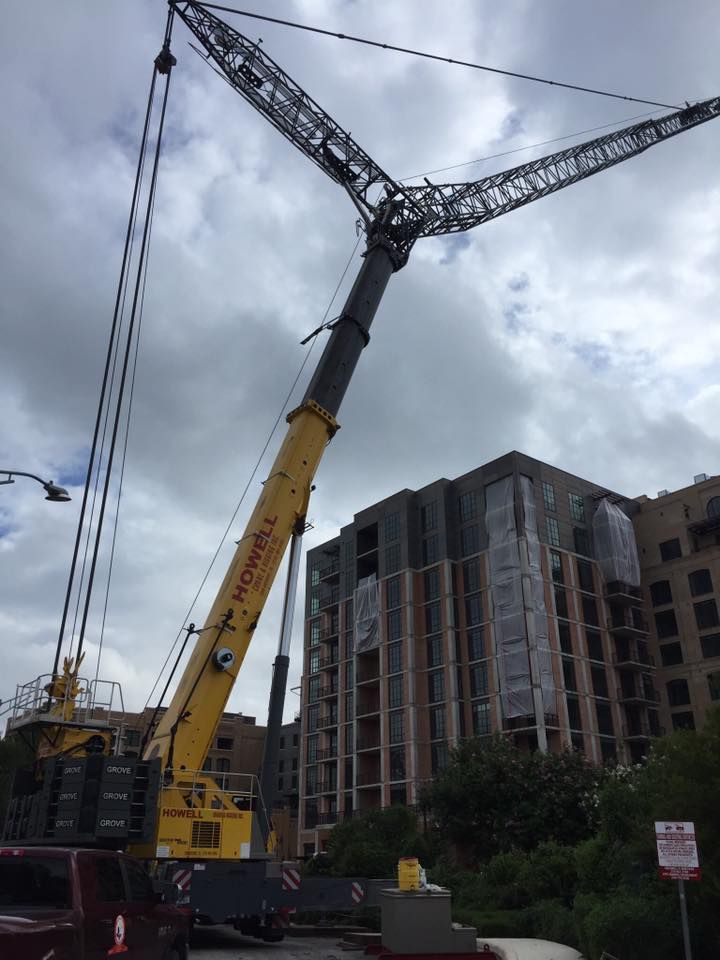 A yellow and black Howell crane next to a building under construction on a cloudy day.