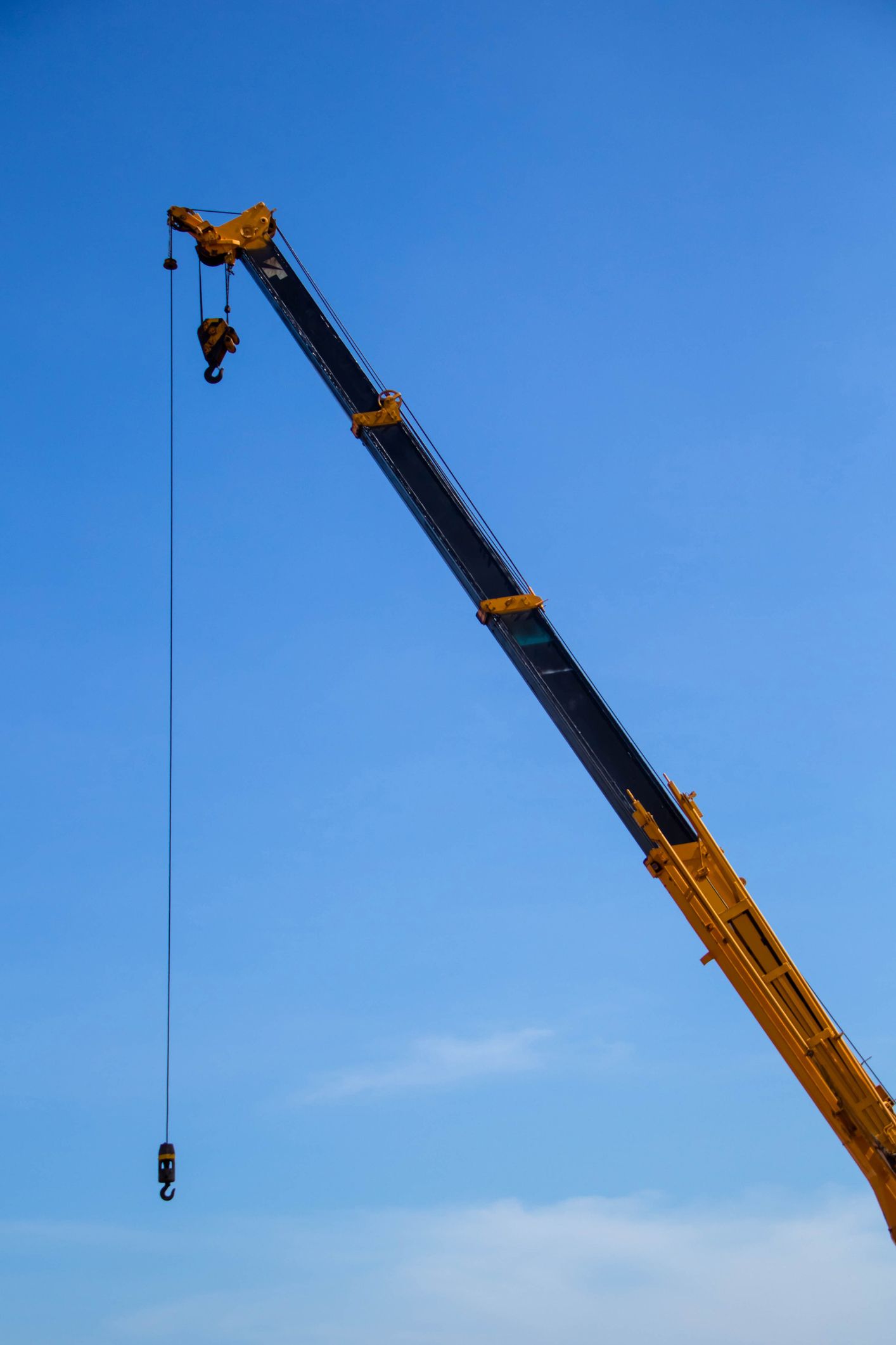 Yellow crane arm against a blue sky, with two suspended hooks.