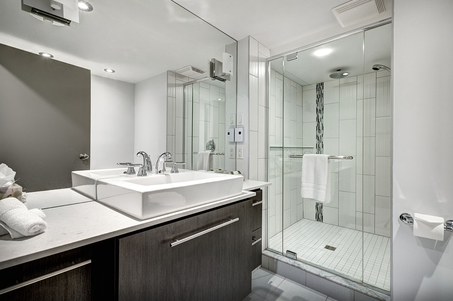 Modern bathroom with white sink, glass shower, gray cabinets, and a large mirror.